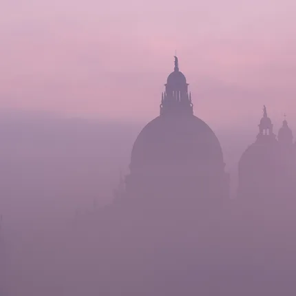 the top of historic buildings peak through the sunrise pink mist.