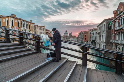 An artist stands on the Accademia Bridge Venice at sunrise painting the beauty of Venice.