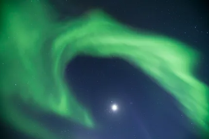 The northern lights sweep around the moon as though they are playing with it