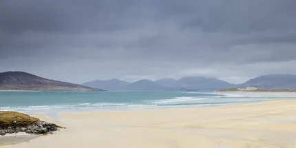 The beach of Seilibost where the colours are like water colours.  Mountains in the background with a moody sky.