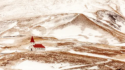 A lone church stands with the barren snow covered landscape of Iceland