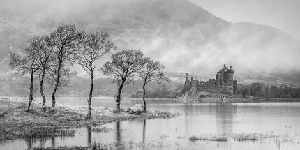 Kilchurn Castle in black and white  ruined stone castle on an Island in Loch Awe. Small trees sit on an island opposite.