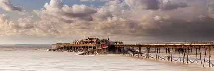An old derelict pier called Birnbeck Pier at Weston Super Mare  with a thunderous clouds building up but  with evening light on the pier itself.