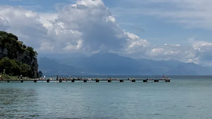 A slender platform stretches into the waters of Lake Garda where sunbathers relax and enjoy the warm Italian sunshine.