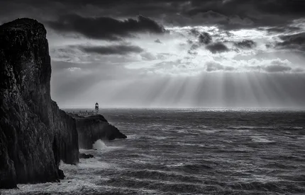 Radiant sunbeams break through clouds above Neist Point.  The lighthouse stands at the edge of the rugged rocks whilst the wild beauty of the Isle of Skye reveals itself. .
