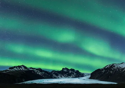 Rays of northern lights shoot over a glacier in an arched way