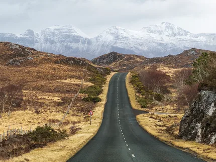 A empty road travels towards the  mountains that are covered in snow in Assynt, Scotland.