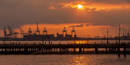 Southampton Docks showing cranes and orange sunset set which reflects into the sea.