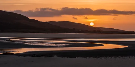 Sunset reflections on the Isle of Skye.  As the sun sets over the mountains it casts  a golden glow in a S-shaped fully that flows towards the sea.