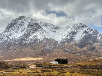 A touch of snow covers the mountains of Glencoe with a small white cottage at the base.