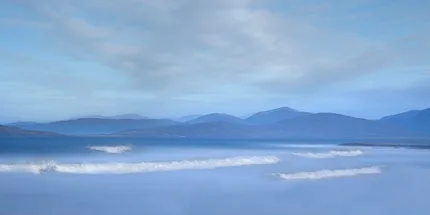 soft waves gently come to the shore with mountains in the background.  Calm Scene
