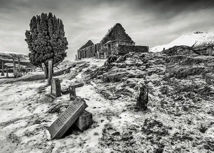 A ruined church with a graveyard in mid winter with snow on the ground.